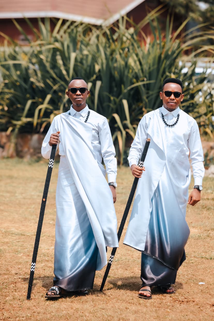 Two grooms in traditional white attire with staffs