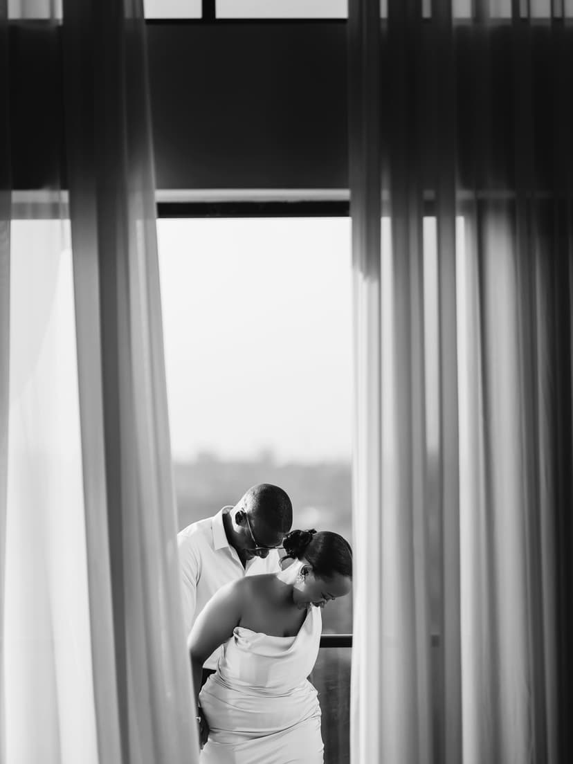 Black and white couple kiss by window with curtains